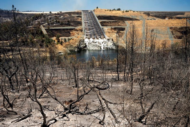 Water flows down the Oroville Dam spillway behind vegetation scorched in the Thompson Fire, in Oroville, Calif., Wednesday, July 3, 2024. An extended heatwave blanketing Northern California has resulted in red flag fire warnings and power shutoffs. (AP Photo/Noah Berger)