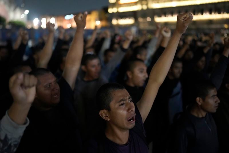 Youths chant, raising their fists in unison, as they take part in a demonstration marking the 10-year anniversary of the disappearance of 43 Ayotzinapa rural teacher's college students, in front of the National Palace in Mexico City, Thursday, Sept. 26, 2024. (AP Photo/Eduardo Verdugo)