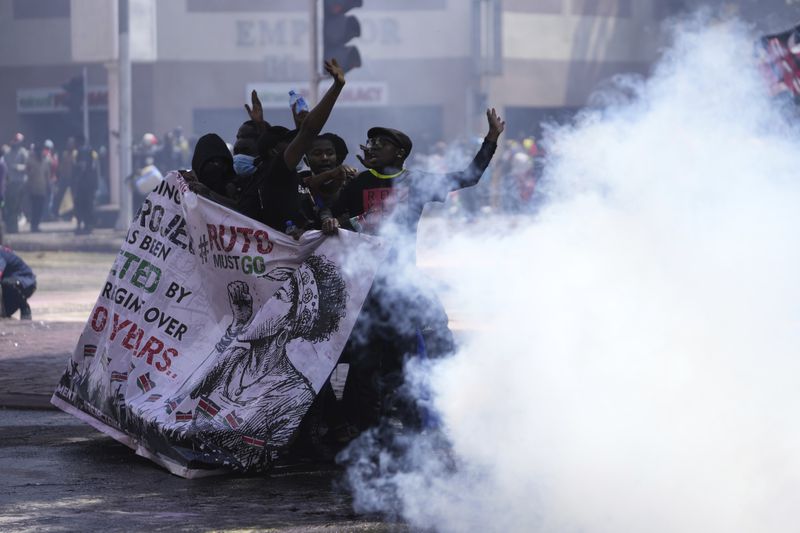 Protesters hide behind a banner as police fire teargas at them during a protest over proposed tax hikes in a finance bill in downtown Nairobi, Kenya Tuesday, June 25, 2024. (AP Photo/Brian Inganga)
