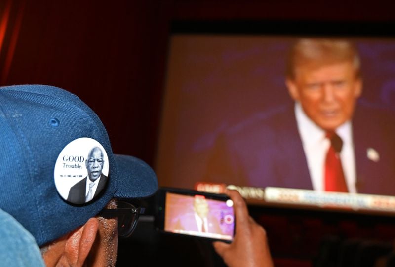 A supporter wearing a John Lewis pin takes a video as he watches the presidential debate between Republican presidential nominee former President Donald Trump and Democratic presidential nominee Vice President Kamala Harris during a Democrat Debate watch party at Tara Theater on Tuesday, Sept. 10, 2024, in Atlanta. The ABC News debate, which begins at 9 p.m., is expected to be the only chance for voters to see the two rivals in a side-by-side confrontation this election season. (Hyosub Shin/AJC)