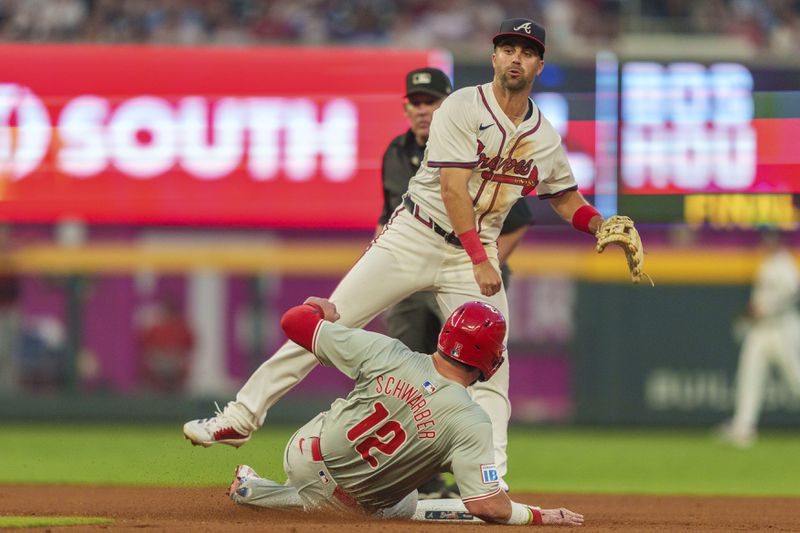 Philadelphia Phillies' Kyle Schwarber (12) slides into second base as Atlanta Braves second baseman Whit Merrifield tags the base and throws to first base to turn a double play in the fourth inning of a baseball game, Wednesday, Aug. 21, 2024, in Atlanta. (AP Photo/Jason Allen)