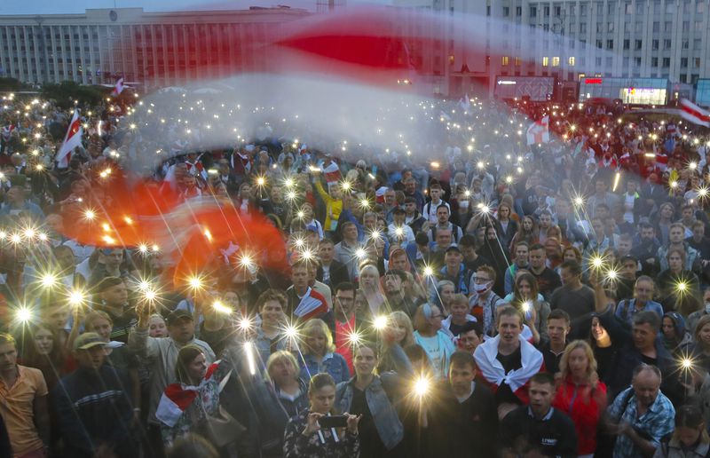 FILE - Protesters shine the lights on their phones and wave red-and-white flags that became symbols of the opposition during an anti-government demonstration in Independence Square in Minsk, Belarus, on Aug. 19, 2020. (AP Photo, File)