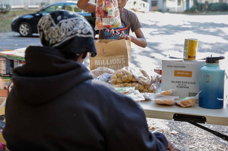 Stacie Jackson, who didn't want her face photographed, waits as a young neighbor fills a bag with food at her apartment complex in south Fulton County on Wednesday, Nov. 1, 2023. A few times a week, Jackson collects food donations and sets up a table with the items to distribute to neighbors in need. (PHOTO by Natrice Miller/ Natrice.miller@ajc.com)