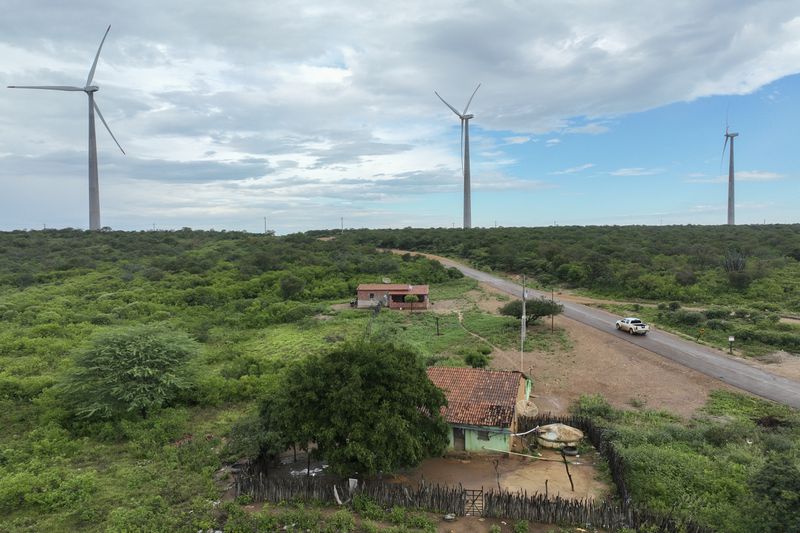 Wind turbines operate near residences in Lagoa, Piaui state, Brazil, Wednesday, March 13, 2024. Wind energy is booming in Brazil's Northeast, but some projects are drawing criticism as it becomes clear that certain communities have benefited while others have not. (AP Photo/Andre Penner)