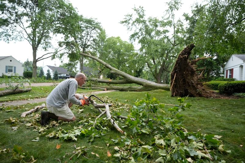 Alan Study cuts a branch near a fallen tree in his front yard Friday, June 21, 2024 in Beverly Hills, Mich. Straight-line winds ripped through tree-lined neighborhoods in portions of Oakland County late Wednesday, leaving residents without power and trees uprooted and tossed across entire streets. (AP Photo/Carlos Osorio)