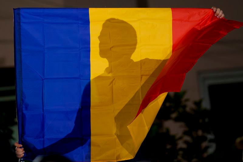 A supporter of the right wing party Alliance for the Unification of Romanians (AUR) holds a flag outside the party headquarters, after the announcement of exit polls in European elections in Bucharest, Romania, Sunday, June 9, 2024. (AP Photo/Vadim Ghirda)