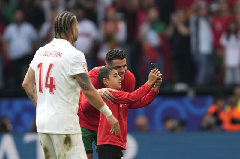 A young pitch invader takes a selfie with Portugal's Cristiano Ronaldo during a Group F match between Turkey and Portugal at the Euro 2024 soccer tournament in Dortmund, Germany, Saturday, June 22, 2024. (AP Photo/Darko Vojinovic)