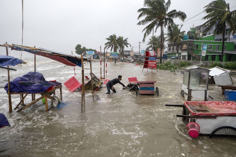 A man salvages a cart and other material as water flows on to the Kuakata beach on the coast of Bay of Bengal because of the advancing Cyclone Remal in Barisal, Bangladesh, Sunday, May 26, 2024. (AP Photo/Abdul Goni)