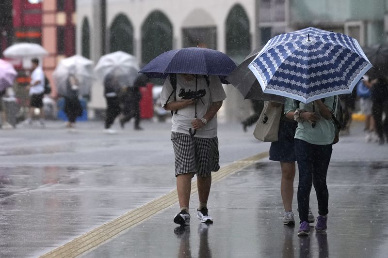 People holding umbrella walk on a street, bracing for a windy and rainy day, as Typhoon Ampil approaches in Tokyo, Japan, Friday, Aug. 16, 2024. (AP Photo/Hiro Komae)