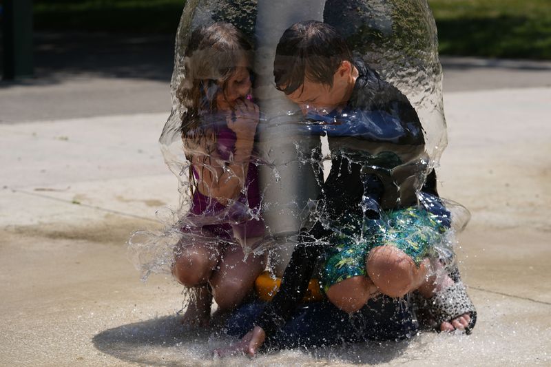 Miles Ruffing and his sister, Frances, play under a water sprinkler while playing at Broad Ripple Park, Friday, June 21, 2024, in Indianapolis. (AP Photo/Darron Cummings)