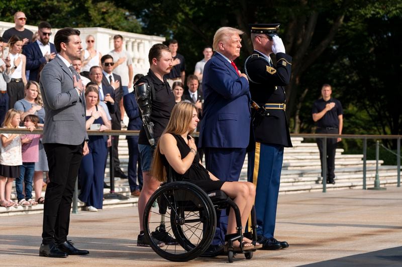 Marlon Bateman, left, former U.S. Marine Sgt. Tyler Vargas, former U.S. Marine Cpl. Kelsee Lainhart, center front, and Republican presidential nominee former President Donald Trump place their hands over their heart after placing a wreath at the Tomb of the Unknown Solider in honor of the 13 service members killed at Abbey Gate, at Arlington National Cemetery, Monday, Aug. 26, 2024, in Arlington, Va. (AP Photo/Alex Brandon)