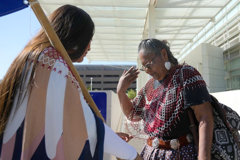 Loveena Watahomigie, left, blesses a tribal member in front of U.S. District Court as they join other members of the Hualapai Tribe gathered to try to persuade a federal judge to extend a temporary ban on exploratory drilling for a lithium project Tuesday, Sept. 17, 2024, in Phoenix. (AP Photo/Ross D. Franklin)