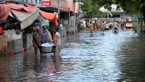 People wade through a flooded road caused by heavy monsoon rain, in Hyderabad, Pakistan, Friday, Aug. 30, 2024. (AP Photo/Pervez Masih)