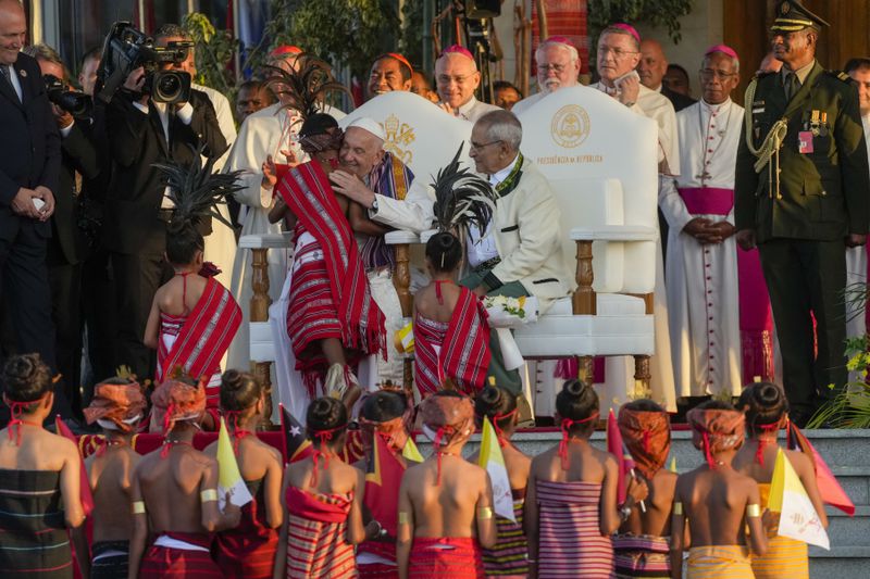 Pope Francis hughs a child in traditional dress as he attends with East Timor's President José Manuel Ramos-Horta, seated at right, a welcome ceremony outside the Presidential Palace in Dili, East Timor, Monday, Sept. 9, 2024. Pope Francis arrived in East Timor on Monday to encourage its recovery from a bloody and traumatic past and celebrate its development after two decades of independence from Indonesian rule. (AP Photo/Gregorio Borgia)