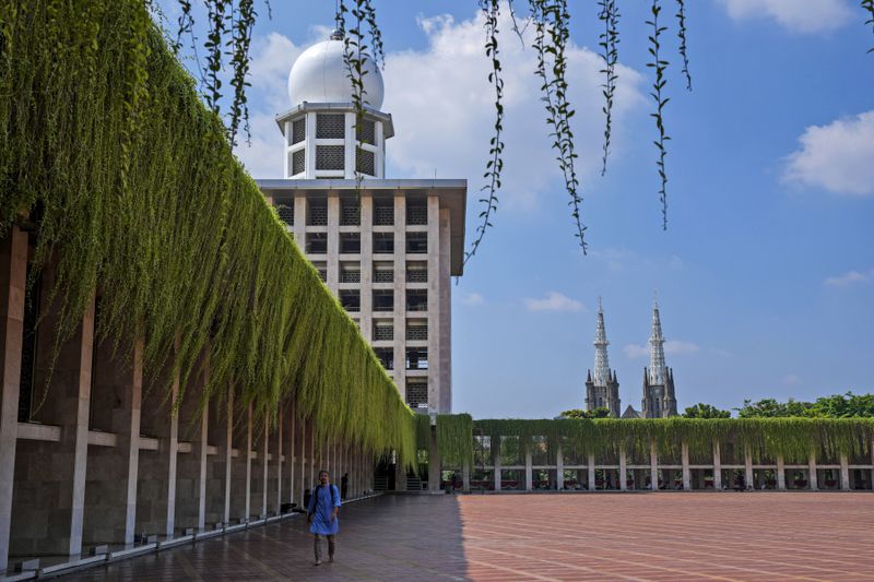 A man walks in the shade at Istiqlal Mosque as the spires of the Our Lady of The Assumption Cathedral are seen in the background, in Jakarta, Indonesia, Friday, Aug. 9, 2024. (AP Photo/Tatan Syuflana)