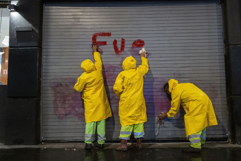 Workers remove a spray painted message accusing the government for the disappearance of 43 Ayotzinapa rural teacher's college students, after a demonstration marking the 10-year anniversary of their disappearance, in Mexico City, Thursday, Sept. 26, 2024. (AP Photo/Jon Orbach)