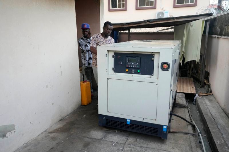 A worker inspects a generator used by Nature's Treat Cafe to run their business in Ibadan, Nigeria, Monday, May 27, 2024. Households and businesses often use polluting gasoline and diesel-run backup private generators. But as fuel prices rise, businesses like Nature's Treat Cafe face unsustainable generator costs, prompting a push for affordable solar solutions. (AP Photo/Sunday Alamba)