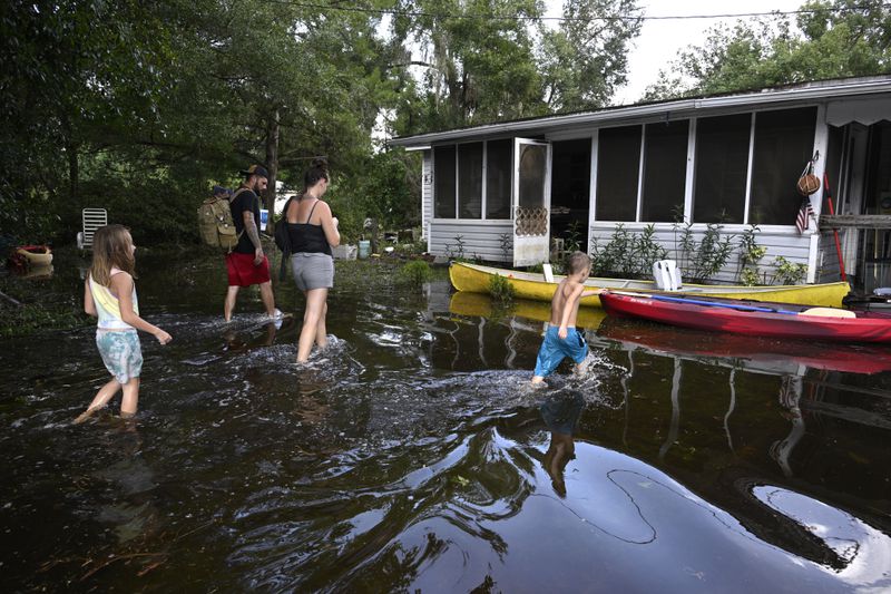 Dustin Holmes, rear, his girlfriend Hailey Morgan, and her children Aria Skye Hall, 7, left, and Kyle Ross, 4, right, arrive to their flooded home in the aftermath of Hurricane Helene, Friday, Sept. 27, 2024, in Crystal River, Fla. (AP Photo/Phelan M. Ebenhack)