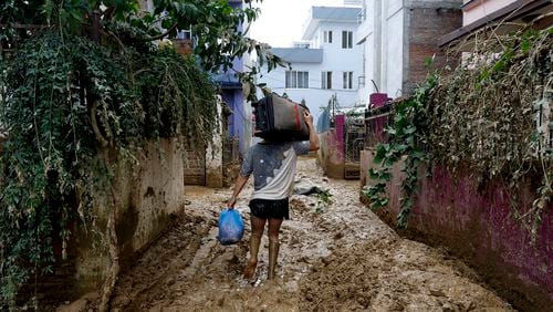 A man walks on a muddy alleyway carrying belongings salvaged from his house in Kathmandu, Nepal, Monday, Sept. 30, 2024 in the aftermath of a flood caused by heavy rains. (AP Photo/Gopen Rai)