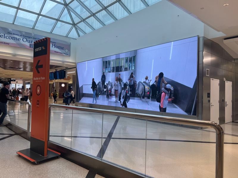 A video screen shows arriving passengers at the top of the escalators at at Hartsfield-Jackson International Airport.