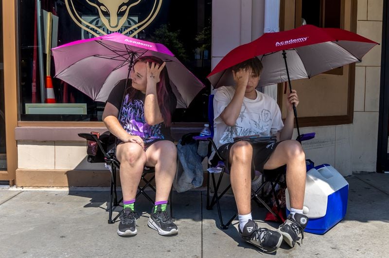 Amanda Gutierrez-19 (left) and her brother, Mateo Gutierrez-17 (right) shade themselves in the heat as they wait for the doors to open at 7PM at the Buckhead Theatre located at 3110 Roswell Road NE in Buckhead on Friday June 14, 2024 after arriving at 9:30 am to see D4VD My House is not a Home Tour. Saturday is forecast to be 97 degrees, and Sunday, Father’s Day will see 95 degrees. (John Spink/AJC)