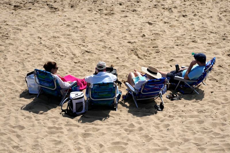 People sit on the beach, Friday, Aug. 30, 2024, in Dennis Port, Mass. (AP Photo/Michael Dwyer)