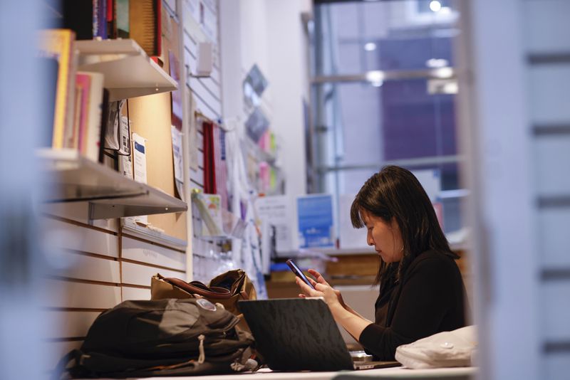 Beatrice Chen, executive director of Immigrant Social Services, checks her phone inside the Storefront for Ideas, Thursday, Aug. 8, 2024, in New York. (AP Photo/Kena Betancur)