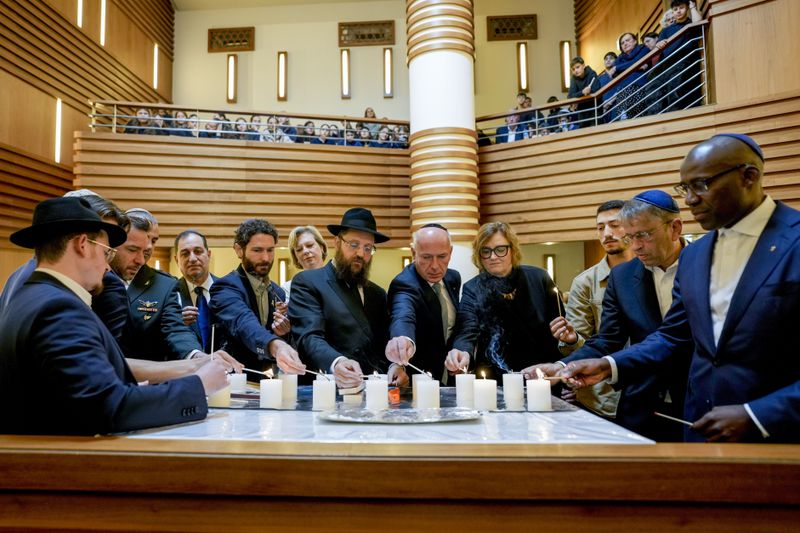 Survivor Alon Gat, Rabi Yehuda Teichtal and Berlin mayor Kai Wegner, centre from left, hold a candle-lighting ceremony marking the first anniversary of the Hamas spearheaded attacks on Israel, at the synagogue of the Chabad community in Berlin, Germany, Monday, Oct. 7, 2024. (AP Photo/Markus Schreiber)