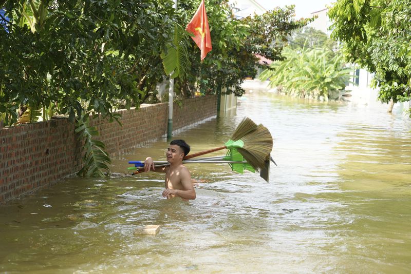 A man wades in flood carrying brooms to clean up houses as flood starts to recede in the aftermath of Typhoon Yagi in An Lac village, Hanoi, Vietnam Friday, Sept. 13, 2024. (AP Photo/Hau Dinh)