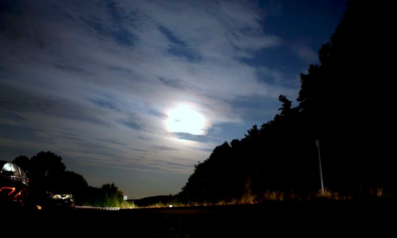 The moon shines over people parked at a scenic overlook to watch for aurora borealis in Alton Bay, New Hampshire as Canada and northern U.S. cities experience moderate solar storms, Thursday, Sept. 12, 2024. (AP Photo/Caleb Jones)