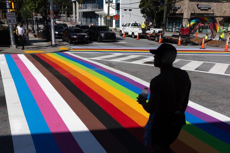 A pedestrian crosses the rainbow crosswalk in Midtown Atlanta on Monday, Oct. 7, 2024. The crosswalk got an inclusive makeover with black and brown stripes for communities of color and the colors of the transgender flag. (Arvin Temkar / AJC)