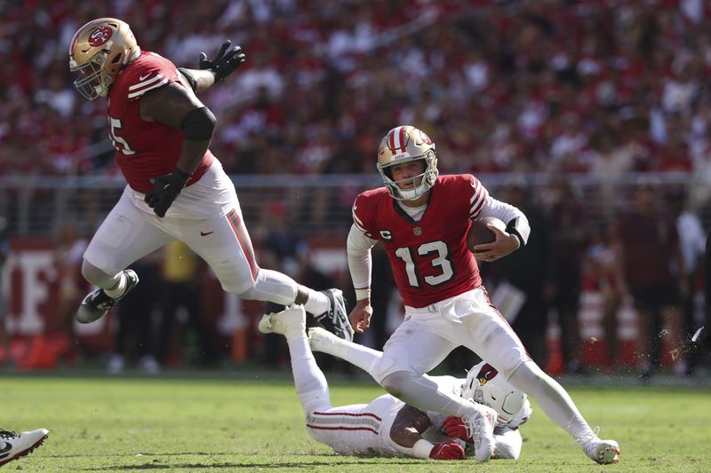 San Francisco 49ers quarterback Brock Purdy (13) runs in front of guard Aaron Banks, top, and Arizona Cardinals linebacker Kyzir White during the second half of an NFL football game in Santa Clara, Calif., Sunday, Oct. 6, 2024. (AP Photo/Jed Jacobsohn)