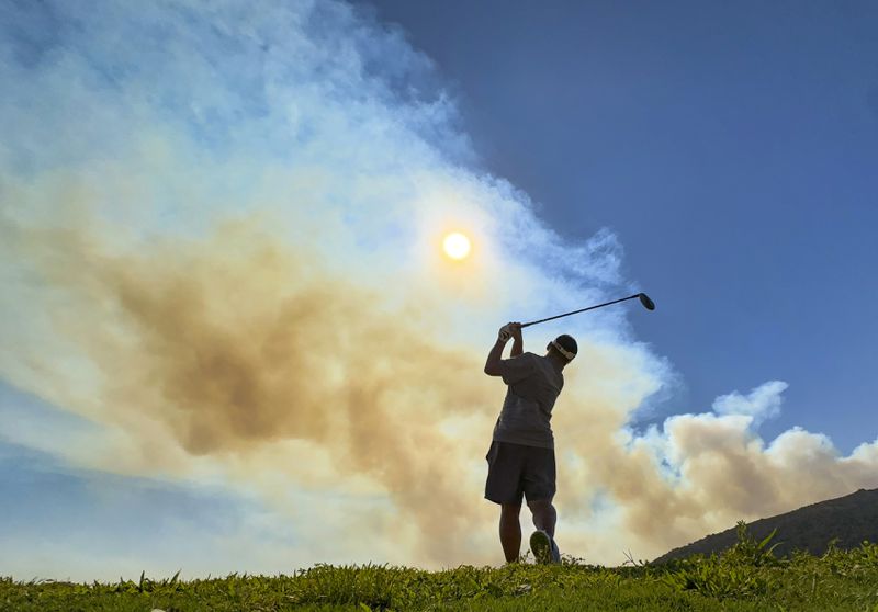 Smoke rises from the Airport Fire as Cizar Moon works out at the driving range at Eagle Glen Golf Club in Corona, Calif., on Tuesday, Sept. 10, 2024. (Jeff Gritchen/The Orange County Register via AP)