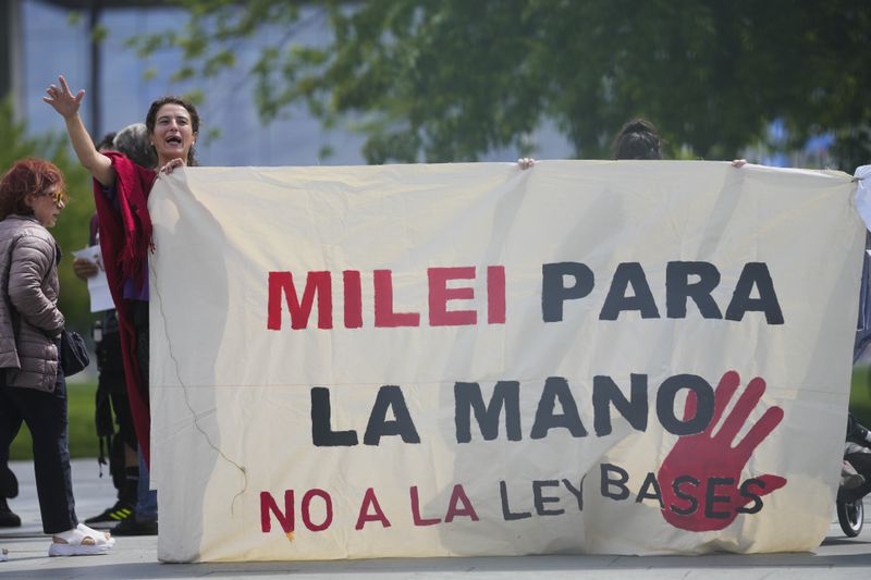Demonstrators show banners and posers as they protest against the visit of Argentina's President Javier Milei for a meeting at the chancellery to meet German Chancellor Olaf Scholz in Berlin, Germany, Sunday, June 23, 2024. Banner reads: Milei for the hand, no to the base law. (AP Photo/Markus Schreiber)