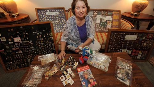 Francis Carey sits on her sofa surrounded by some of her over 1,800 Olympic pins. She got the collecting bug during the 1996 Olympics.