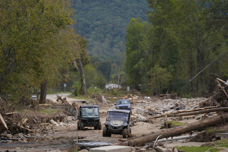 Vehicles roll along on a washed up road in the aftermath of Hurricane Helene, Thursday, Oct. 3, 2024, in Pensacola, N.C. (AP Photo/Mike Stewart)