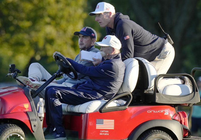 United States team captain Jim Furyk, top, grabs a ride with United States team member Keegan Bradley, left, and Mike "Fluff" Cowan driving during their fourth-round foursomes match at the Presidents Cup golf tournament at Royal Montreal Golf Club, Saturday, Sept. 28, 2024, in Montreal. (Frank Gunn/The Canadian Press via AP)