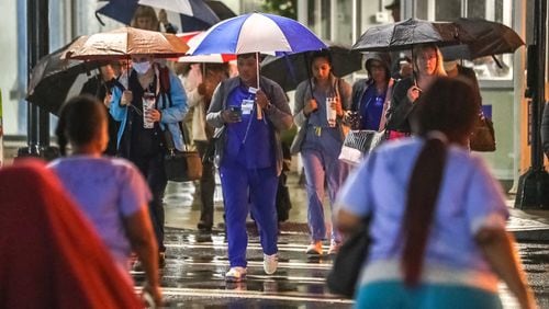 Health care workers walk to Emory University Hospital in the rain Thursday along West Peachtree Street and Linden Avenue.