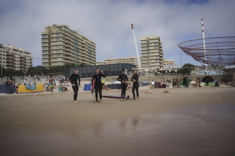 Surf Church members, from left, Zakharii Yarovyi, Lydia Fleete, Ian Carsoso and Lais Cardoso, cheer on their pastor, the Rev. Samuel Cianelli, as he catches a wave in Matosinhos beach in the suburbs of Porto, Portugal on Sunday, Aug. 18, 2024. (AP Photo/Luis Andres Henao)