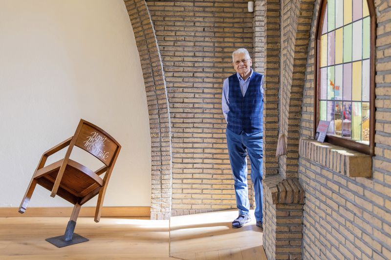 Rik Deville, a retired priest, poses next to a church chair with a message written in Dutch saying "No More Abuse" at the Don Bosco church in Buizingen, Belgium, Sunday, Sept. 8, 2024. (AP Photo/Geert Vanden Wijngaert)