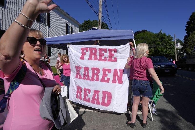 Eva Jenkins, of Bourne, Mass., left, a supporter of Karen Read, waves to passing cars as other supporters place a banner, right, a block away from Norfolk Superior Court, Tuesday, June 25, 2024, in Dedham, Mass. Karen Read is on trial, accused of killing her boyfriend Boston police Officer John O'Keefe, in 2022. (AP Photo/Steven Senne)