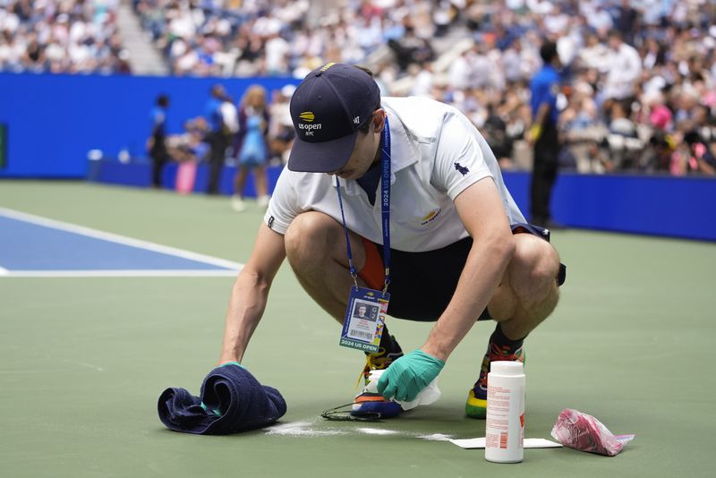 Court attendant Ethan Davison cleans up an area on the court where Jack Draper, of Great Britain, vomited in the second set against Jannik Sinner, of Italy, during the men's singles semifinal of the U.S. Open tennis championships, Friday, Sept. 6, 2024, in New York. (AP Photo/Frank Franklin II)