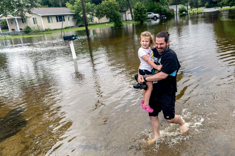 Ryan Tolbert, of Davison, carries his daughter Fiona, 4, through flood waters while walking back to their car after picking her up from his sister's house following rains from the remnants of Hurricane Beryl, Wednesday, July 10, 2024, in Genesee Township, Mich. "It's insane. I can't even describe it," Tolbert said. "I've never seen anything like this. It blows my mind." (Jake May/The Flint Journal via AP)