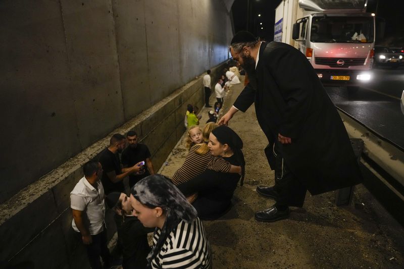 People take cover on the side of a road as a siren sounds a warning of incoming missiles on a freeway in Shoresh, Israel Tuesday, Oct. 1, 2024. (AP Photo/Ohad Zwigenberg)