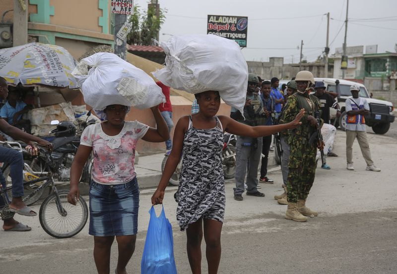 Pedestrians cross a street as Kenyan police officers patrol an area near the international airport, in Port-au-Prince, Haiti, Wednesday, July 3, 2024. (AP Photo/Odelyn Joseph)