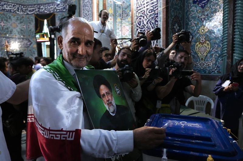 A man casts his ballot during the presidential election as he holds a picture of the late President Ebrahim Raisi in a polling station, in Tehran, Iran, Friday, June 28, 2024. Iranians were voting Friday in a snap election to replace the late President Ebrahim Raisi, killed in a helicopter crash last month, as public apathy has become pervasive in the Islamic Republic after years of economic woes, mass protests and tensions in the Middle East. (AP Photo/Vahid Salemi)