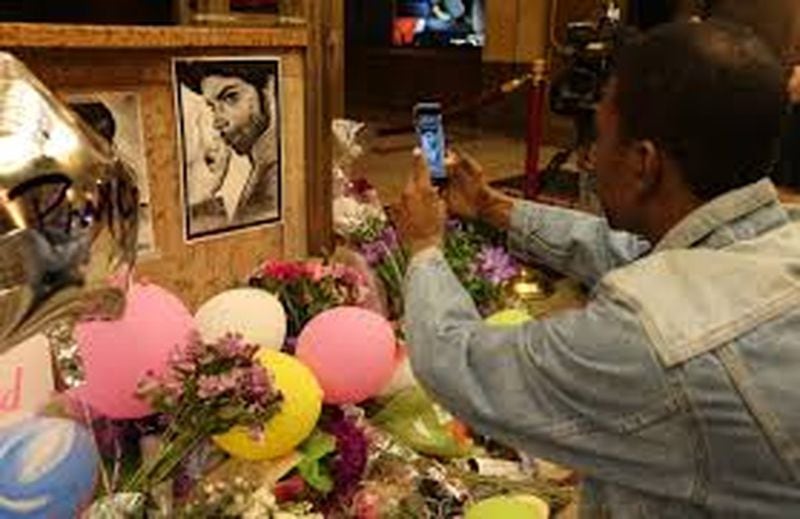Michael Glover of Atlanta takes a photograph of the Prince memorial in front of the Fox Theatre on April 22, 2016. The musician played his final public concert at the Fox a week before he died. BEN GRAY / BGRAY@AJC.COM