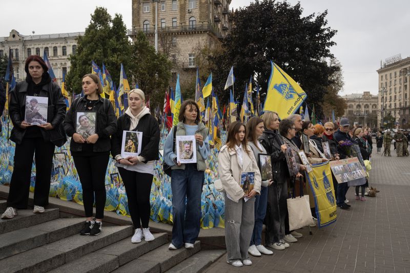 People hold photos of their relatives soldiers to keep a nationwide minute of silence in memory of fallen soldiers, who defended their homeland in war with Russia, on Defenders Day at the improvised war memorial in Independence square in Kyiv, Ukraine, Tuesday, Oct. 1, 2024. (AP Photo/Efrem Lukatsky)