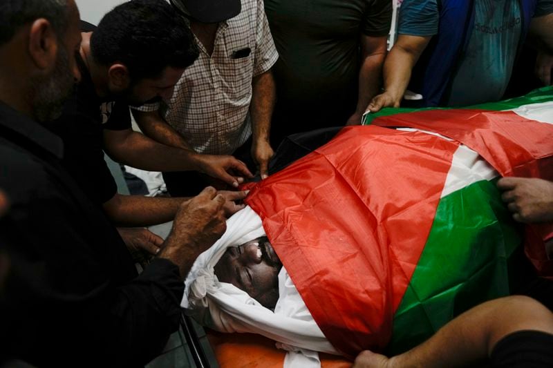 Mourners take a last look at Khalil Ziada, wrapped with a Palestinian flag, who died during an Israeli settler attack in the Wadi Rahal village, at a hospital morgue in the West Bank city of Bethlehem, Tuesday, Aug. 27, 2024. (AP Photo/Mahmoud Illean)