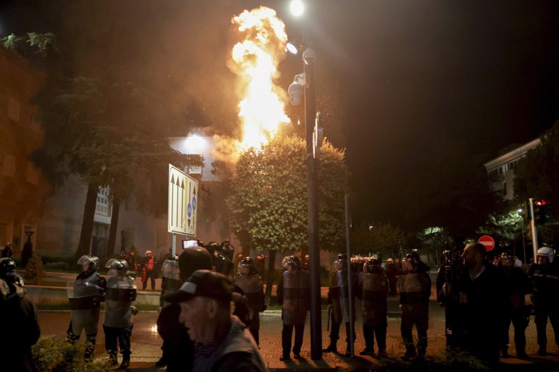 Fire burns behind a riot police cordon during an anti-government rally set up by the opposition, in Tirana, Albania, Monday, Oct. 7, 2024. (AP Photo/Hameraldi Agolli)